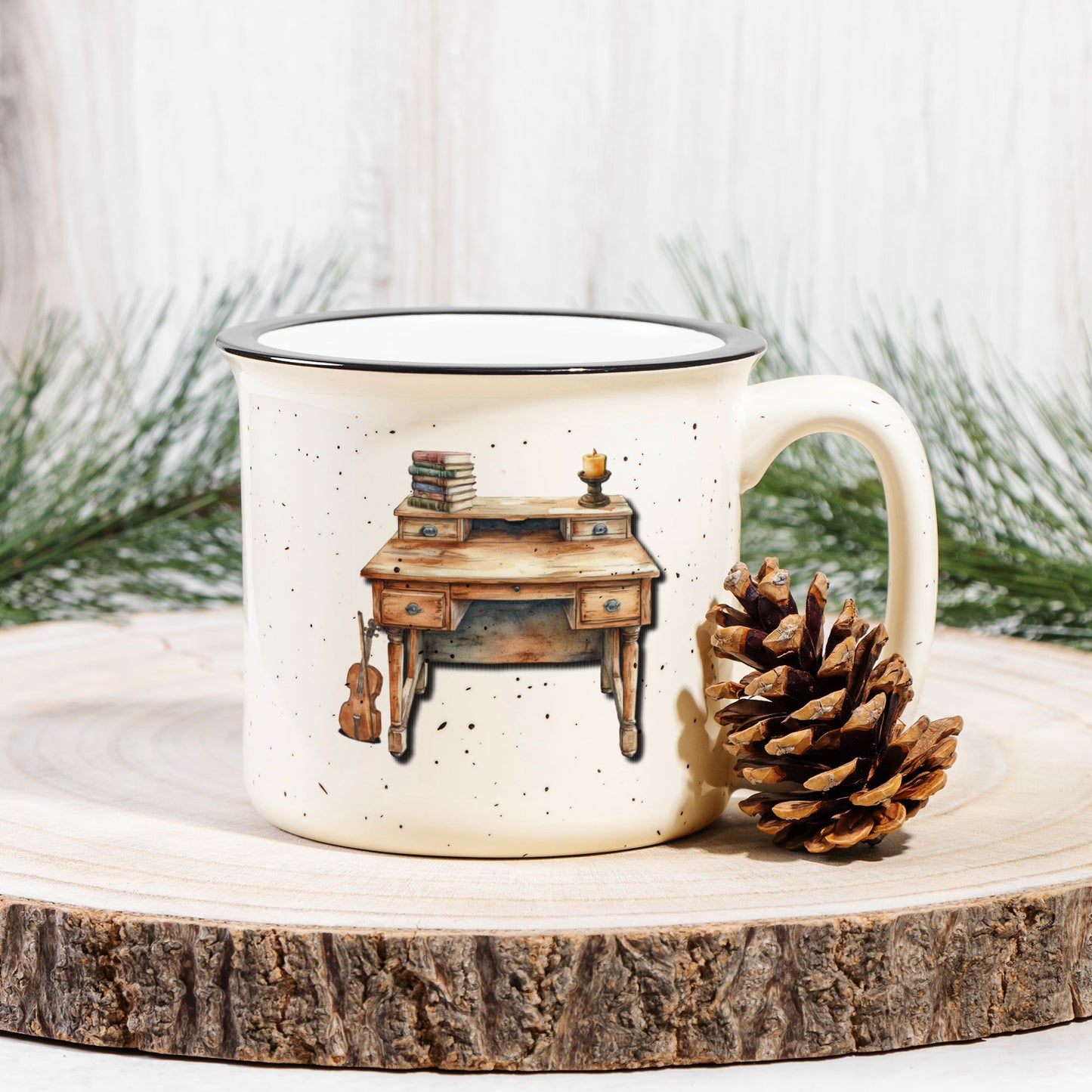 Mug with a desk illustration on a wooden surface with a pine cone and evergreen branches.