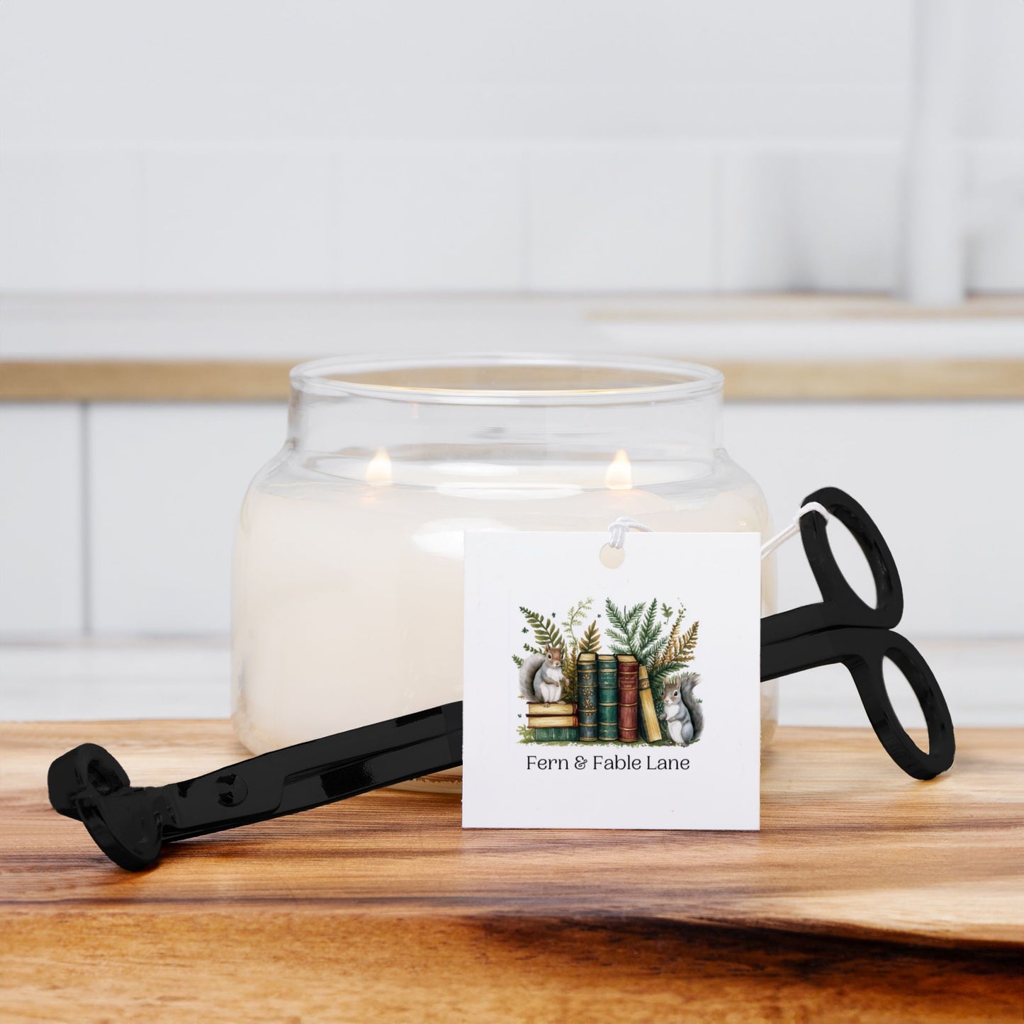 Glass candle jar with a decorative label and black wick trimmer  on a wooden surface.