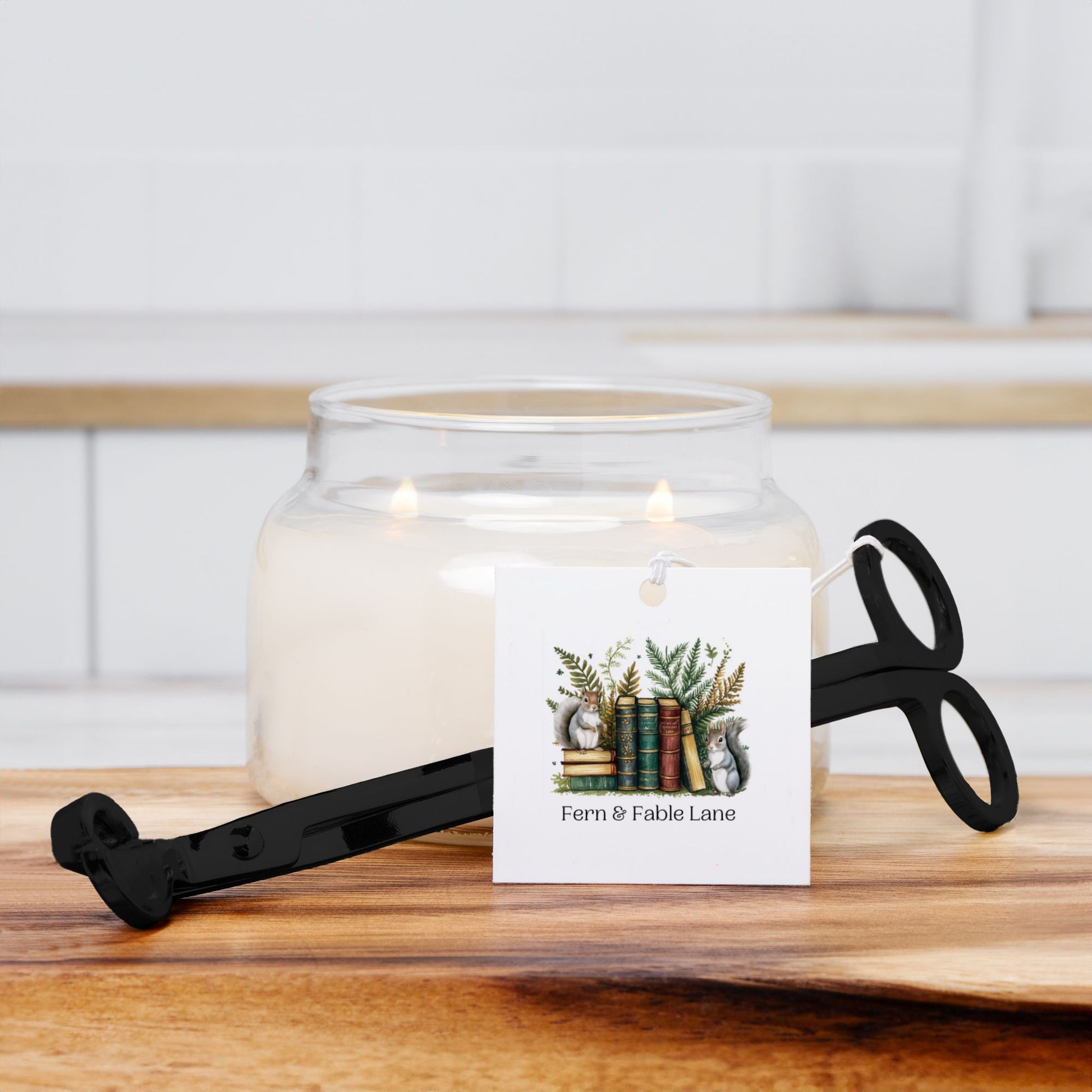 Glass candle jar with a decorative label and black wick trimmer  on a wooden surface.