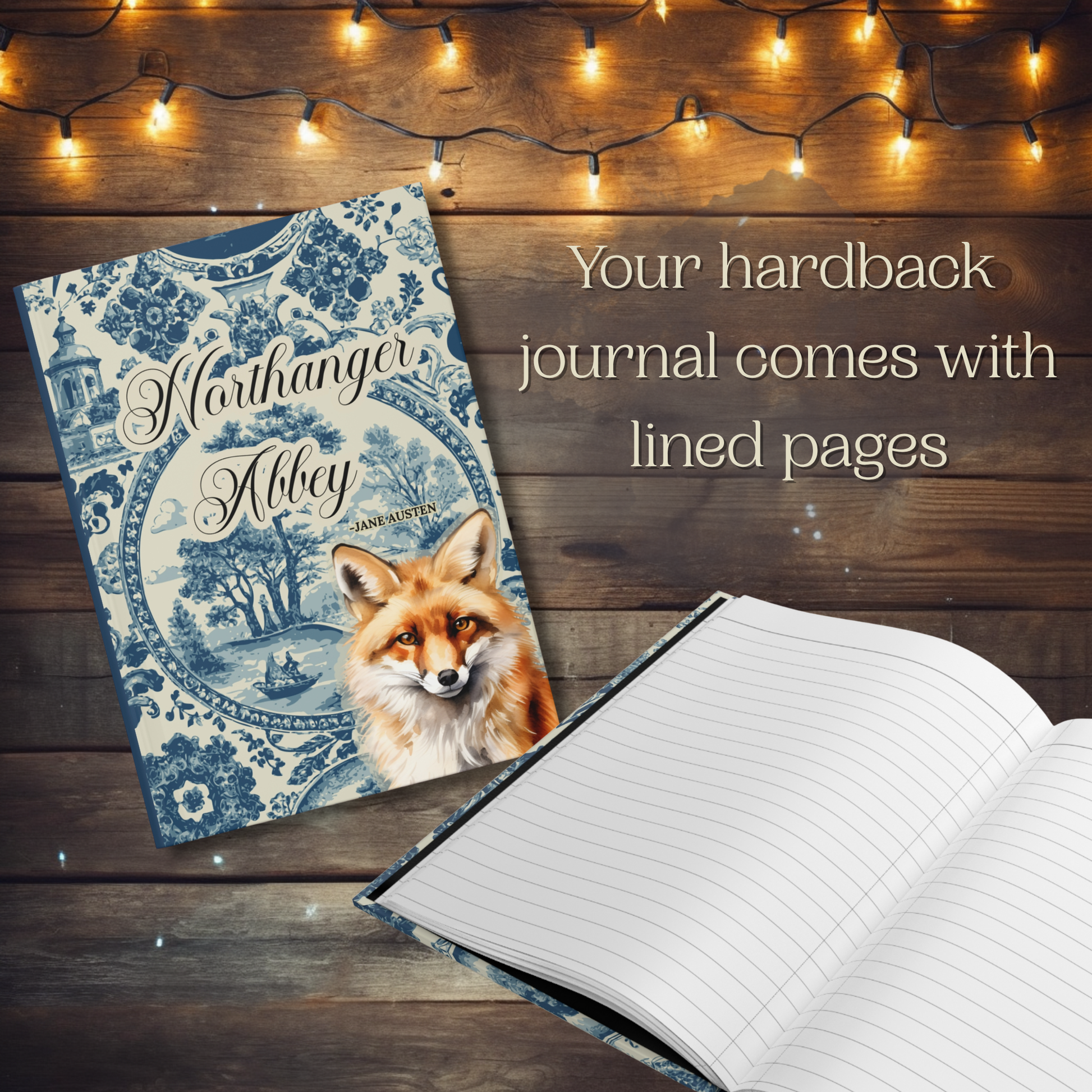 Hardback journal with fox illustration on wooden surface with string lights. Text reads, "Your hardback journal comes with lined pages."