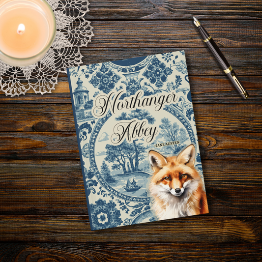 Notebook titled 'Northanger Abbey' with a fox illustration on a wooden surface with a candle and pen.