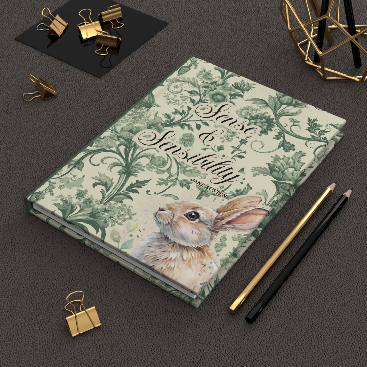 Notebook with rabbit illustration and 'Sense & Sensibility' text on a dark surface with stationery items.