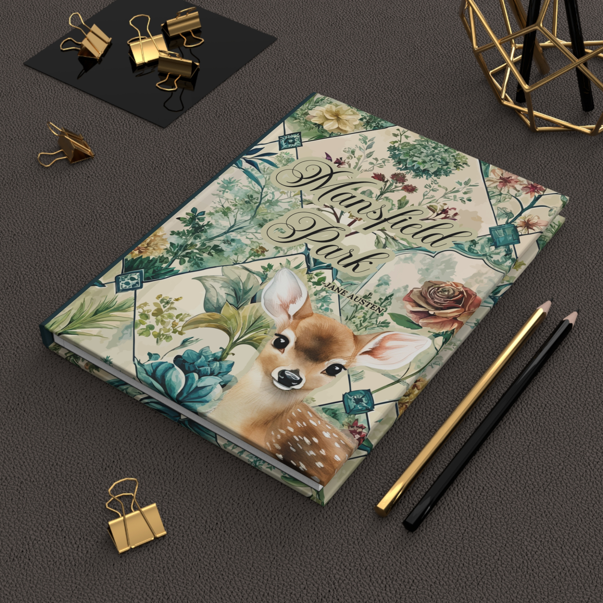 Notebook with floral and deer design on a dark surface with stationery items.