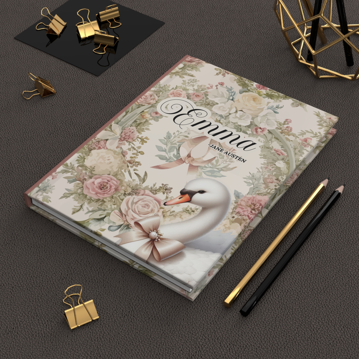 Notebook with floral design and swan illustration on a dark surface with stationery items.
