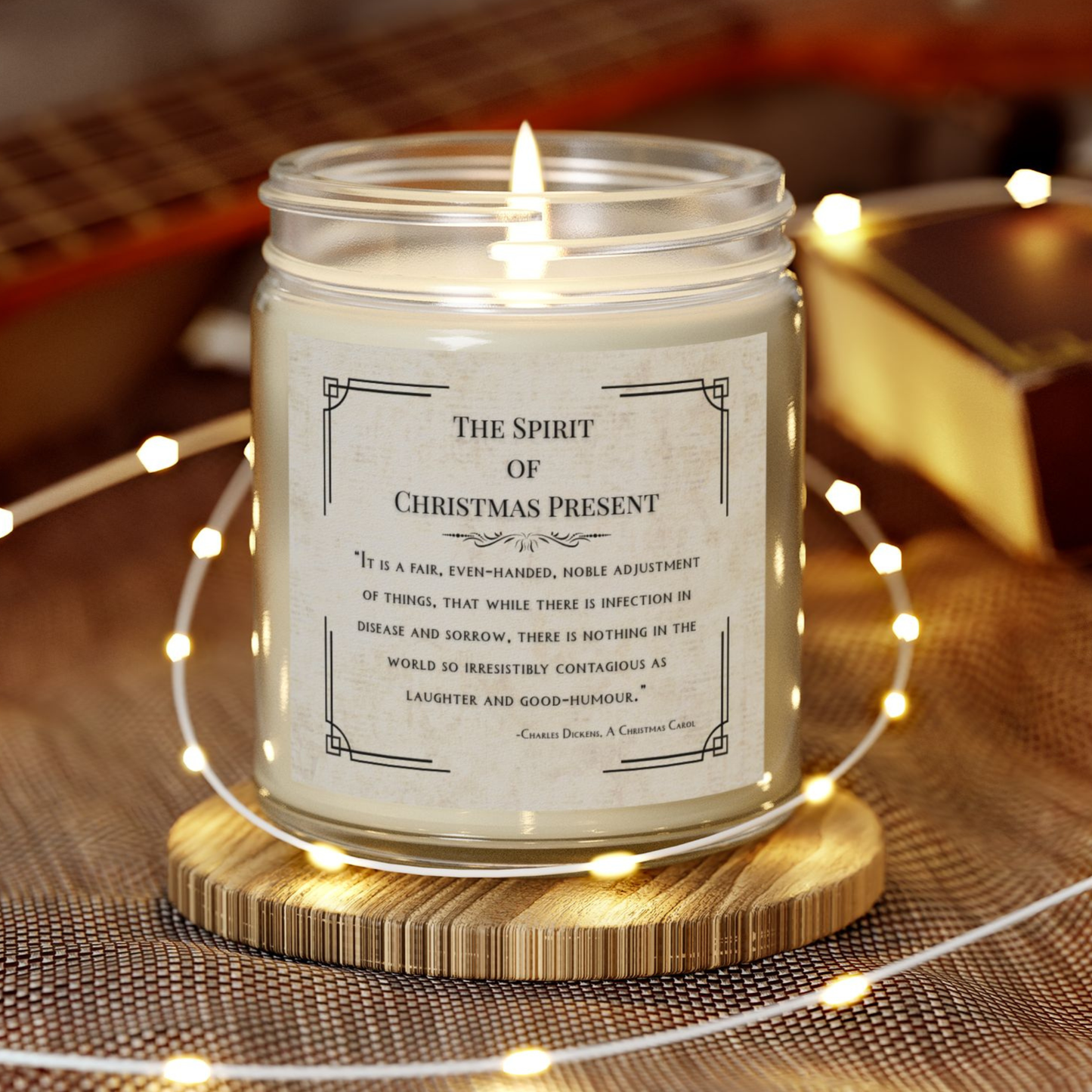 Candle in a jar with a label titled 'The Spirit of Christmas Present' on a wooden coaster with string lights.