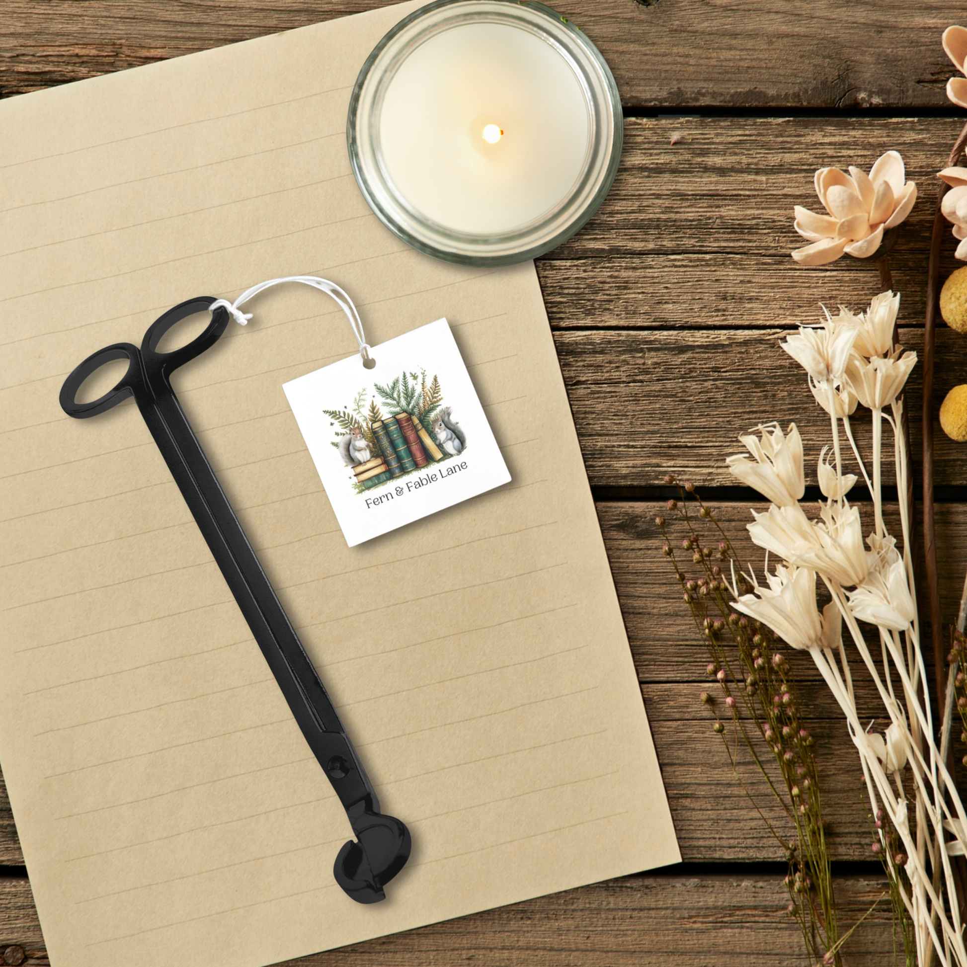 Wick trimmer, a candle, and a tag on a wooden surface with flowers.